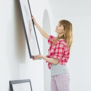 Woman hanging picture frame on wall in new house